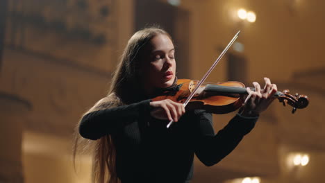 classic-music-concert-in-philharmonic-hall-young-female-violinist-is-playing-fiddle-in-dark