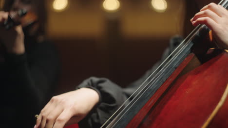 female-violoncellist-in-orchestra-on-scene-of-philharmonic-hall-closeup-of-cello-bow-and-hands-of-cellist