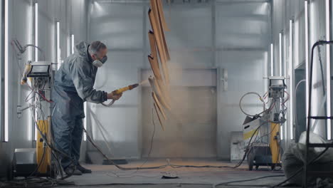 A-man-in-a-protective-suit-and-mask-sprays-paint-through-a-spray-gun-in-slow-motion-on-steel-parts.