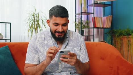 Indisch-arabischer-Junger-Mann-Zu-Hause-Nutzt-Smartphone-Und-Feiert-Erfolg,-Sieg-Und-Sieg,-Spielt-Online-Spiel