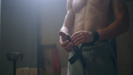 Young-athletic-Caucasian-man-changing-putting-weight-lifting-straps-on-in-gym-locker-room-before-workout-slow-motion.-ties-arms-to-barbell-with-fitness-straps.