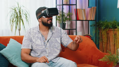 Indian-man-using-virtual-reality-futuristic-technology-headset-play-simulation-3D-video-game-at-home