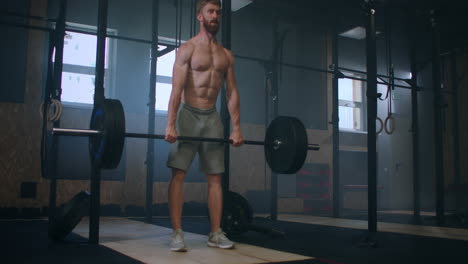 Wide-shot-of-young-Caucasian-extreme-weightlifting-athlete-man-working-out-with-heavy-barbell-in-large-hardcore-gym-hall.