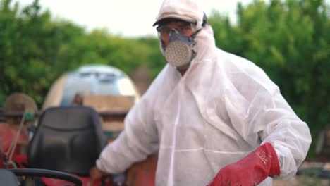 Farmer-wearing-protective-gloves-while-spraying-pesticide-on-lemon-trees-with-tractor