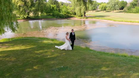 Aerial-Shot---Caucasian-newlyweds-walking-on-grass-near-a-pond