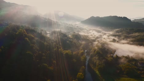 aerial-drone-view-of-river-in-the-middle-of-a-forest-with-mist-at-golden-hour-in-morning,-hill-and-mountain-in-background,-tuscany,-italy,-europe
