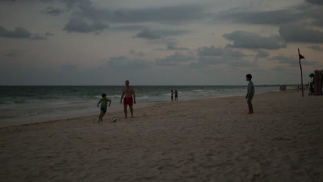 Papa-Spielt-Mit-Seinen-Kindern-Fußball-An-Einem-Weißen-Sandstrand-Mit-Kristallklarem-Meer-In-Cancun,-Mexiko
