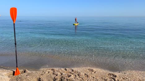 Mädchen-Beim-Pfützensurfen-Im-Meer-In-Nerja-Malaga,-Stand-Up-Pfützenboarden-An-Einem-Sonnigen-Tag-In-Spanien,-Lustige-Urlaubsaktivität,-Abenteuerlicher-Wassersport,-Statische-4K-Aufnahme