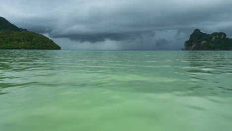 low-flying-aerial-dolly-above-shimmering-green-water-to-stormy-grey-black-clouds-above-ocean,-koh-phi-phi-thailand