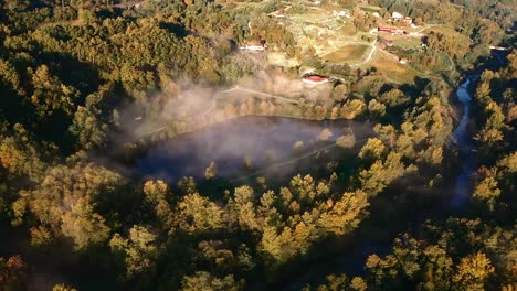 lake-in-forest-with-mist-at-golden-hour-in-morning,-aerial-drone-bird-zenithal-view,-hill-and-mountain-in-background,-tuscany,-italy,-europe