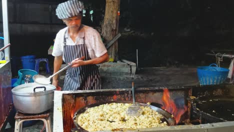 Thailändischer-Streetfood-Koch-Tanzt,-Während-Er-Frisch-Gebratene-Muschelpfannkuchen-Auf-Einer-Brennenden-Pfanne-In-Ayutthaya,-Thailand,-Zubereitet