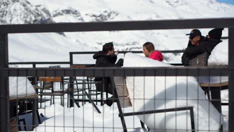 Chairs-of-a-store-completely-buried-in-snow,-people-enjoying-a-beer-with-a-view-of-the-Farellones-park-Chile