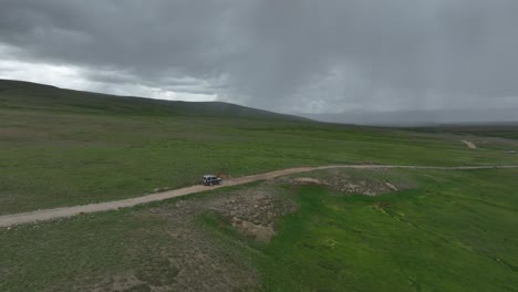Aerial-shot-of-a-passenger-jeep-moving-on-the-road-in-the-vast-plains-of-Deosai-National-Park,-Pakistan-with-dark-clouds-in-the-sky