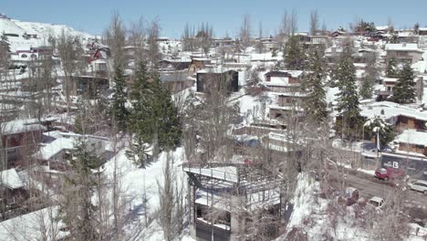 Aerial-view-dolly-in-establishing-of-the-mountain-village-of-Farellones,-luxury-cabins-with-local-materials-and-trees-with-snow-and-without-leaves,-Chile