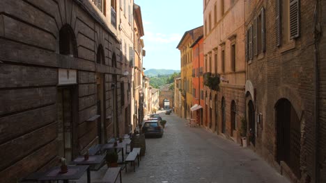 Pan-shot-of-an-empty-old-street-with-rows-of-old-buildings-on-both-sides-in-Urbino,-Italy-on-a-sunny-day