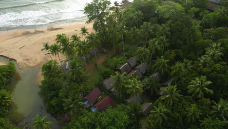 Aerial-shot-looking-down-on-homes-in-Thailand-as-waves-crash-on-the-beach