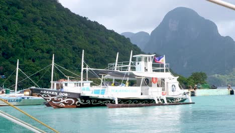Philippinisches-Inselhüpfen-Tourboot-Mit-Philippinischer-Flagge-Im-Hafen-Von-El-Nido-Angedockt,-Mit-Blick-Auf-Tropische-Inseln-Im-Hintergrund