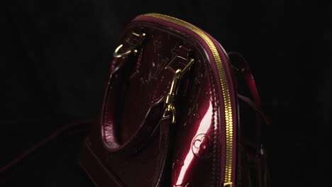 Dark-red-glossy-Louis-Vuitton-handbag-turning-with-black-background,-expensive-luxury-product-made-of-leather,-famous-brand,-4K-shot