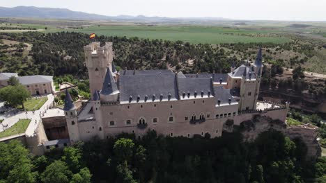 Daytime-aerial-pan-of-grand-Alcazar-of-Segovia-fortress-on-rocky-crag,-Spain