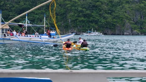Group-of-kayakers-selling-cold-drinks-and-coconuts-to-tourist-on-island-hopping-tour-boats-in-El-Nido,-Palawan,-Philippines