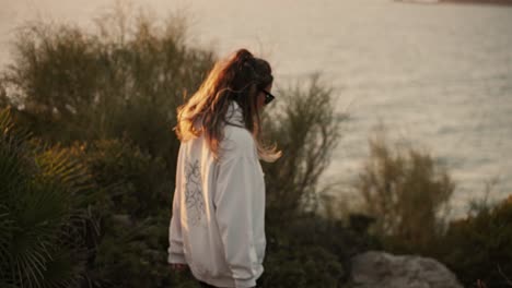 Young-girl-walking-determinedly-in-slow-motion-along-a-cliff-with-the-sea-in-the-background