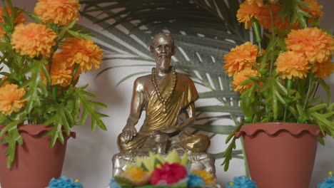Buddhistische-Statue-Auf-Einem-Regal-Zwischen-Orangefarbenen-Blumen