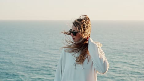 Slow-motion-shot-of-a-girl's-hair-being-blown-over-her-face-at-the-ocean-during-sunset