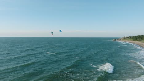 Establishing-aerial-view-of-a-group-of-people-engaged-in-kitesurfing,-sunny-summer-day,-high-waves,-extreme-sport,-Baltic-Sea-Karosta-beach-,-wide-drone-shot-moving-forward
