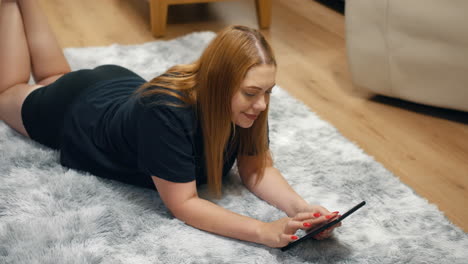 A-woman-relaxing-at-home-laying-on-a-rug-using-a-tablet-in-a-living-room