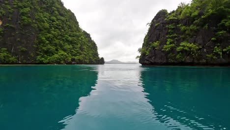 Passing-rugged-and-rocky-tropical-islands-on-a-boat-in-calm,-placid-and-pristine-turquoise-ocean-water-in-Palawan,-Philippines