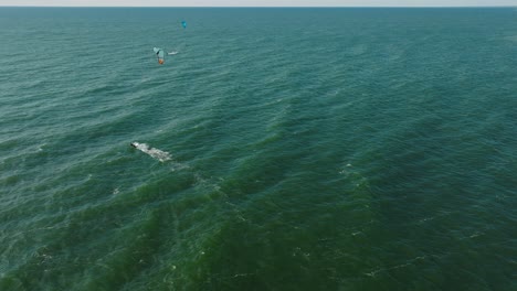 Establishing-aerial-view-of-a-group-of-people-engaged-in-kitesurfing,-sunny-summer-day,-high-waves,-extreme-sport,-Baltic-Sea-Karosta-beach-,-wide-drone-shot-moving-forward,-tilt-down