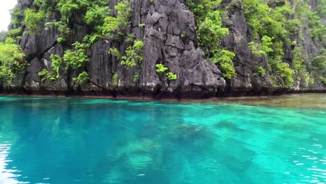 Black-rugged-and-rocky-tropical-island-with-steep-cliffs-into-crystal-clear-turquoise-ocean-water-in-Palawan,-Philippines