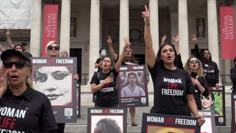 Protesters-holding-placards-that-depict-Mahsa-Amini-and-others-that-have-been-killed-in-women’s-rights-protests-in-Iran-stand-on-steps-in-Trafalgar-Square-and-give-the-peace-sign