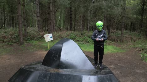 Funny-alien-giving-peace-sign-standing-on-flying-saucer-in-Rendlesham-forest-woodland