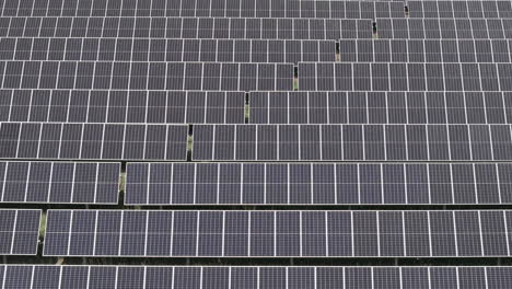 Aerial-up-close-view-of-large-solar-farm-with-many-rows-of-solar-panels-creating-green,-renewable-energy-to-replace-fossil-fuels-and-to-power-clean-transition-to-fight-climate-change