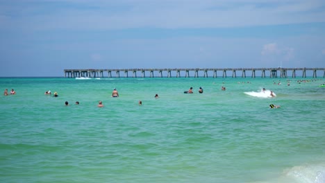 Beach-with-People-swimming-in-the-turquoise-water-of-gulf-of-mexico-with-fishing-pier-in-the-background