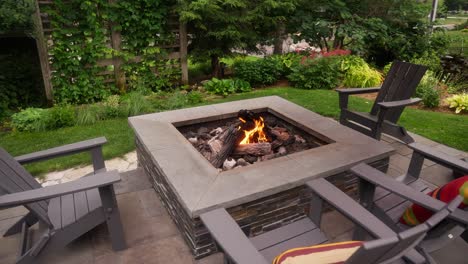 orbiting-shot-of-a-propane-fire-pit-with-a-roaring-flame-surrounded-by-chairs-on-a-patio-during-the-day
