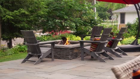 static-shot-of-a-patio-seating-area-that-includes-a-propane-fire-pit-surrounded-by-adirondack-chairs