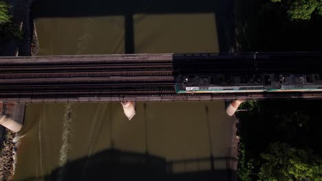 Via-Rail-train-crossing-river-bridge-with-dramatic-evening-lighting,-overhead-aerial-shot