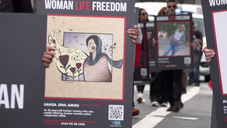 Demonstranten,-Die-Whitehall-Entlang-Marschieren,-Halten-Plakate-In-Der-Hand,-Auf-Denen-Mahsa-Amini-Und-Andere-Menschen-Abgebildet-Sind,-Die-Bei-Frauenrechtsprotesten-Im-Iran-Getötet-Wurden