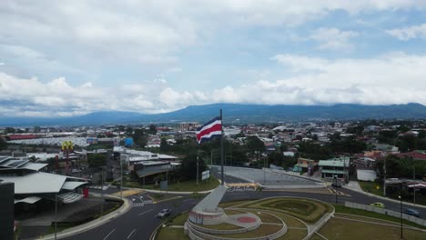 Drone-Flying-Towards-Costa-Rican-Flag-in-the-middle-of-Roundabout-with-Beautiful-View-of-Mountains-in-the-Background