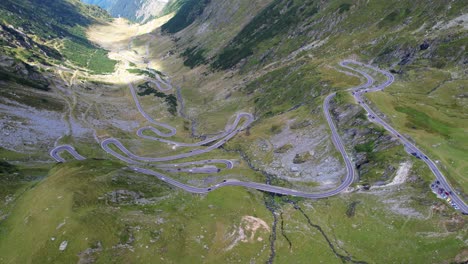 Cars-quickly-drive-switchback-winding-busy-road-of-Transfagarasan-Serpentine-highway-in-romania,-under-shadow-of-mountain-peaks