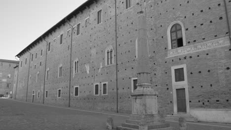 Schwarz-Weiß-Aufnahme-Von-Touristen,-Die-Tagsüber-Um-Das-Gebäude-Herumlaufen,-Das-Das-Geburtshaus-Des-Malers-Raphael-In-Der-Unesco-Altstadt-Von-Urbino,-Italien-Ist