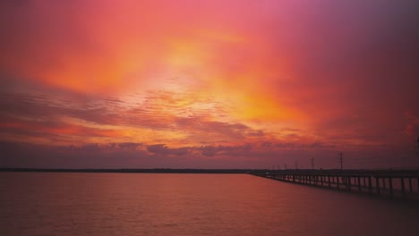 Epische-Wolkenlandschaft-Mit-Leuchtend-Orangeroten-Farbtönen-Bei-Sonnenuntergang-über-Dem-Fluss-An-Der-Autobahnbrücke