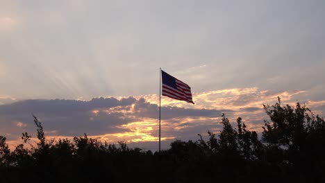 Yellow-sunset-rays-in-pink-blue-sky-behind-clouds-frame-patriotic-waving-american-flag