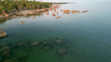 Aerial-pan-over-water-to-coastline-with-boulders,-Lake-Huron,-Michigan