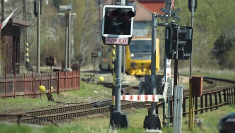 Ein-Bahnübergang-Ist-Gesperrt-Und-Die-Signale-Blinken,-Während-Der-Zug-Am-Bahnhof-Wartet
