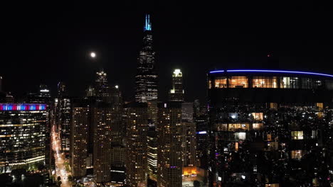 Glossy-apartment-building,-full-moon-above-the-West-Loop,-Chicago-skyline---Aerial-view