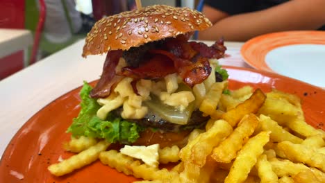 Cheeseburger-with-crispy-bacon,-pickles,-lettuce-and-fries,-unhealthy-restaurant-food-experience,-4K-shot