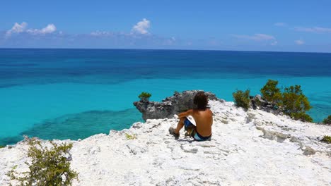 Static-video-of-a-young-boy-looking-out-from-a-cliff-into-the-ocean-in-Exuma-in-the-Bahamas